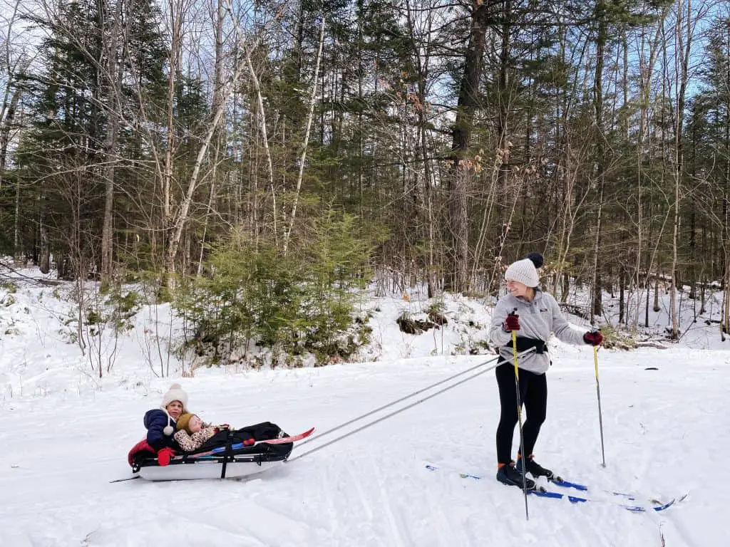 Cross-country skier mom and child on sled at Carter's XC Ski Center